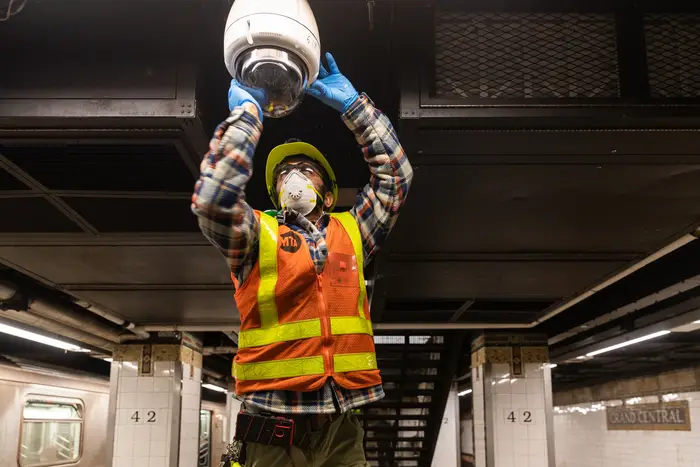 A stock photo of an MTA worker cleaning a subway camera.